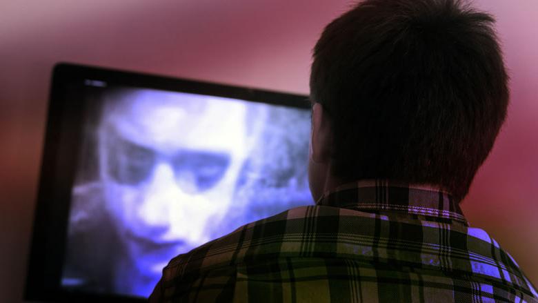 Image of the back of a viewers head while he watches a black and white zombie movie